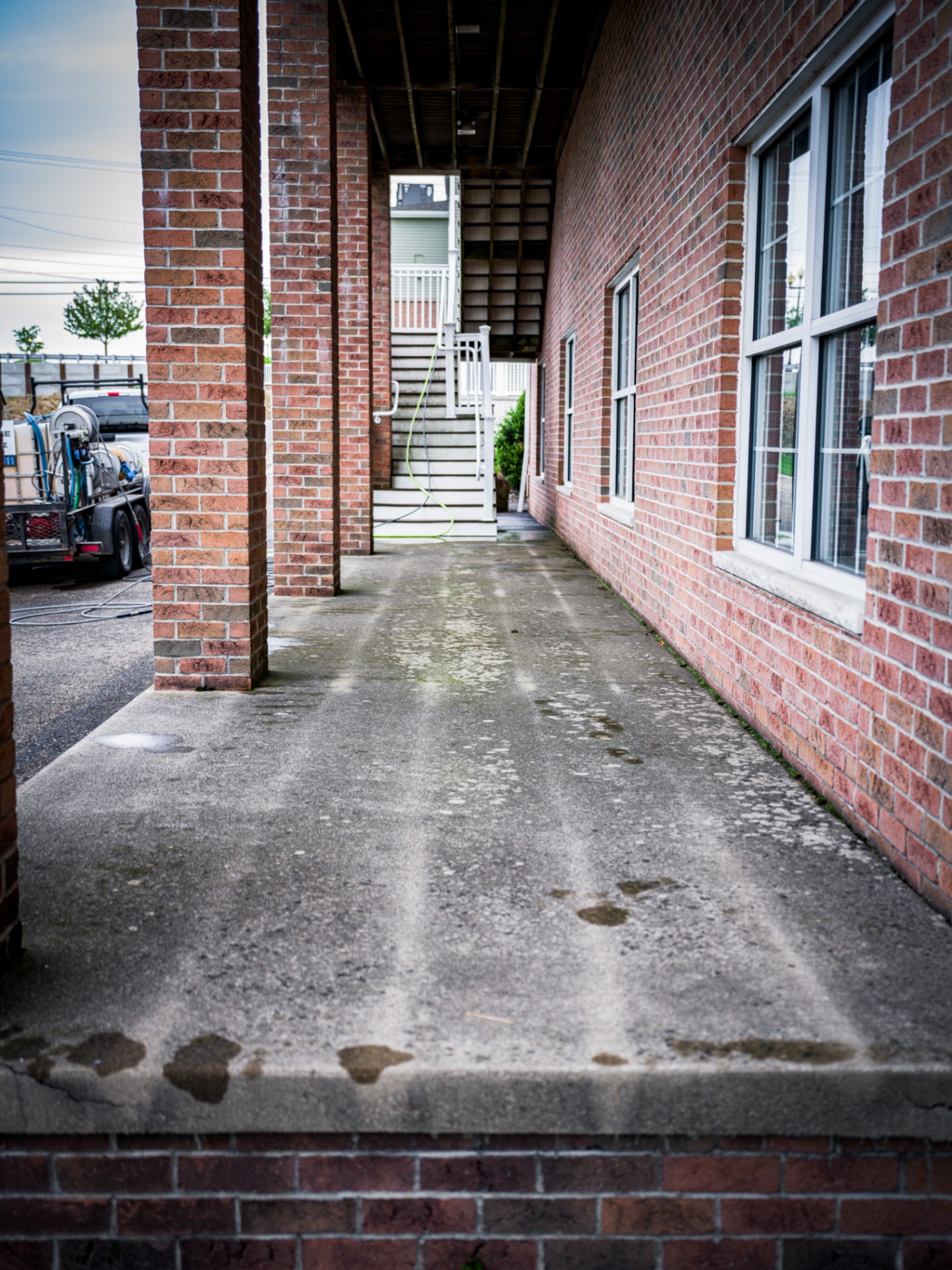 Dirty concrete walkway between brick building and stairs before pressure washing