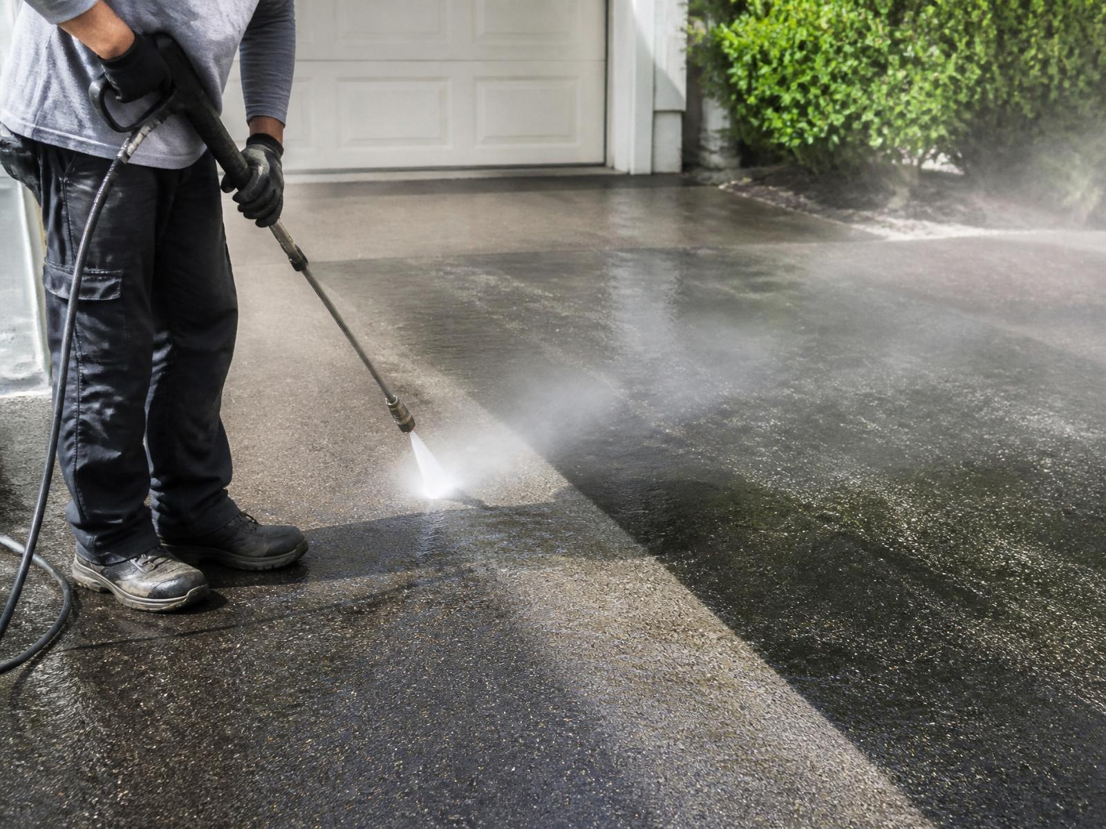 Pressure washer cleaning a concrete driveway revealing clean surface